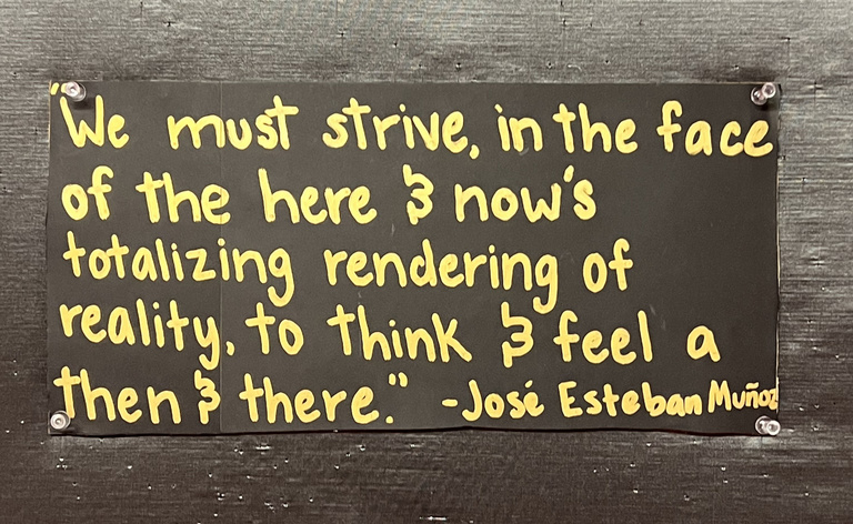 Handwritten quote in yellow letters on a black background: "We must strive, in the face of the here and now's totalizing rendering of reality, to think and feel a then and there." by Jose Esteban Nunoz