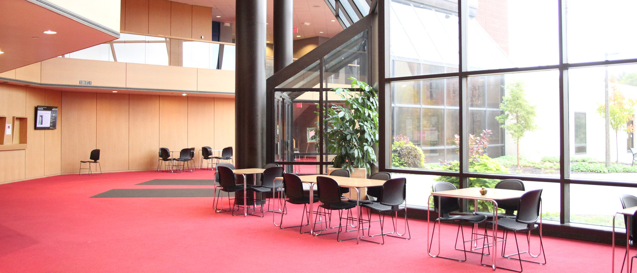 Image of Theatre Building lobby. Large glass windows, tables and chairs, red carpet.